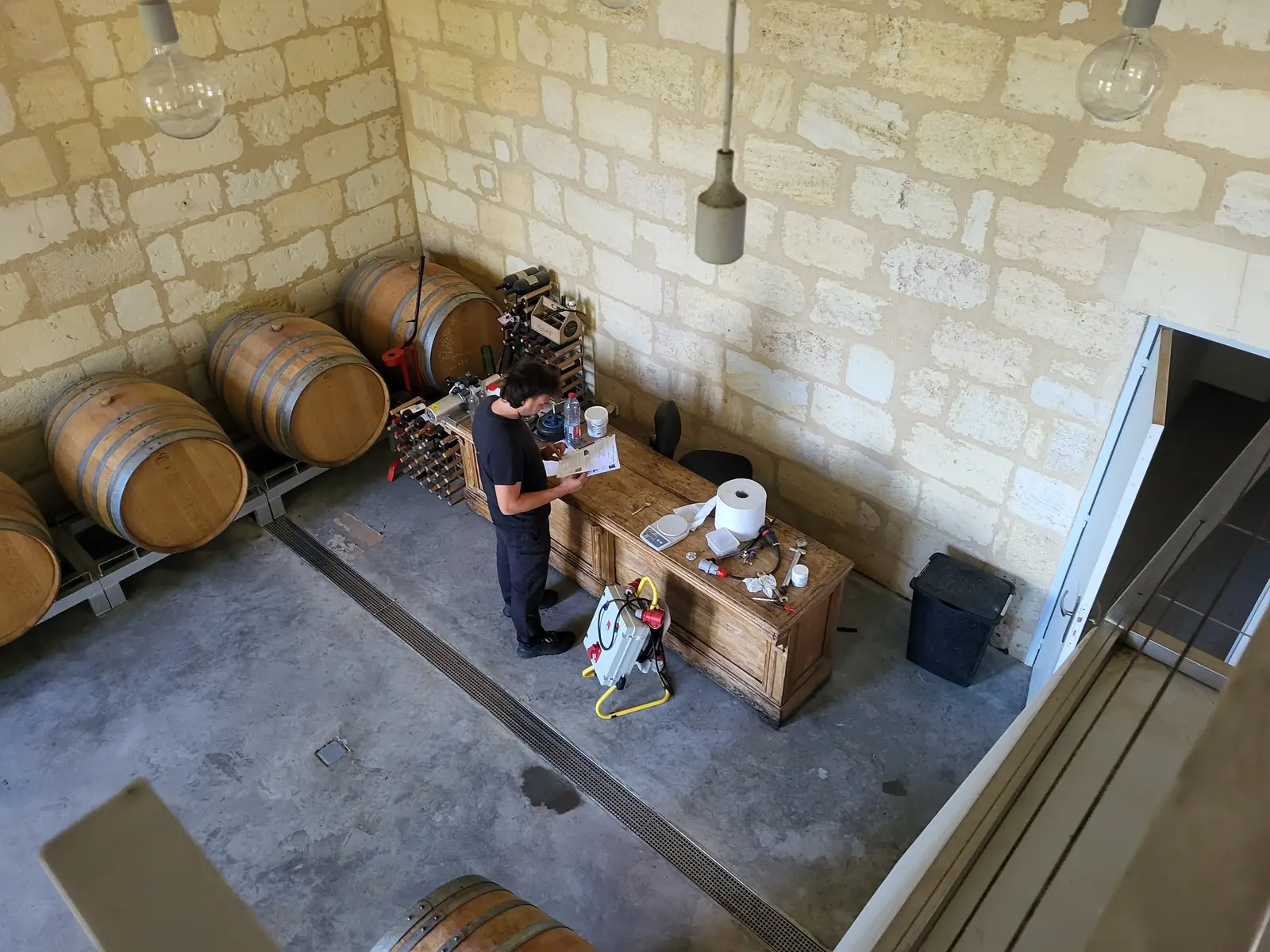 Chai à barriques en vue plongeante — Laurent Giraud, Gironde Vue plongeante sur un chai à barriques en pierre où un ouvrier de chai prépare ses analyses