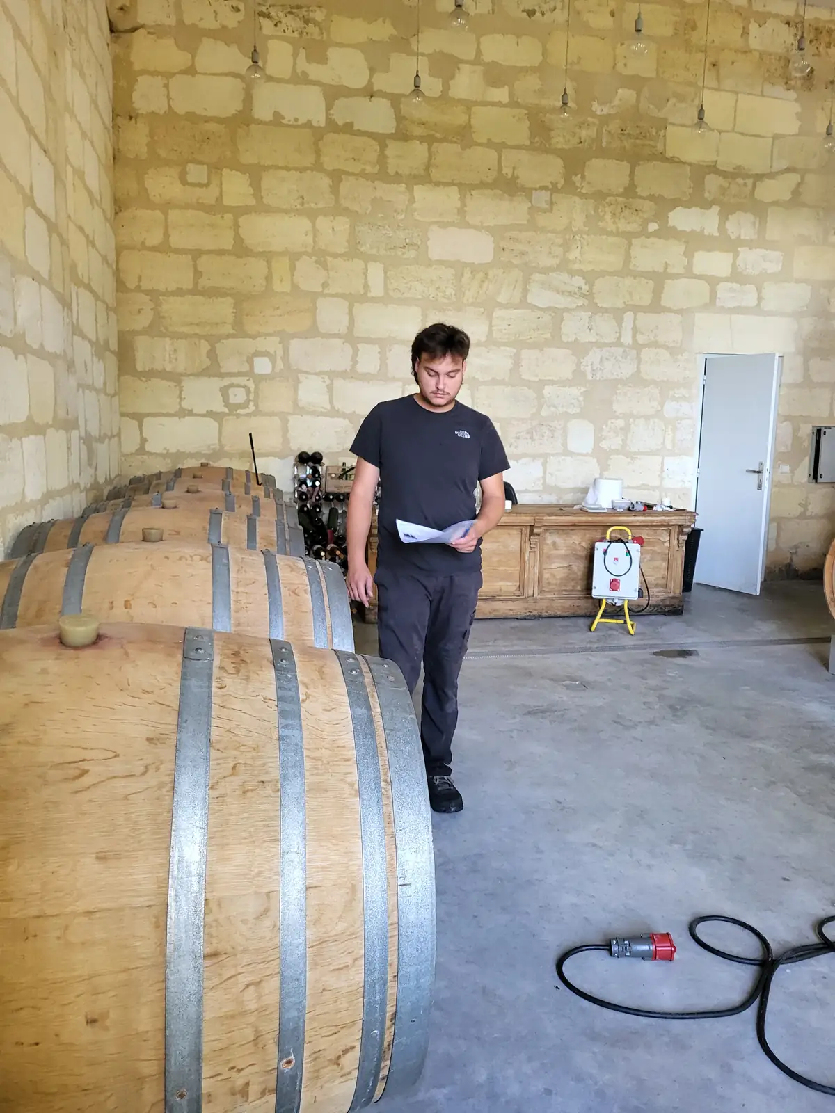 Ouvrier de chai au chai à barriques — Laurent Giraud, Gironde Ouvrier de chai consultant sa fiche de travail dans un chai à barriques en pierre